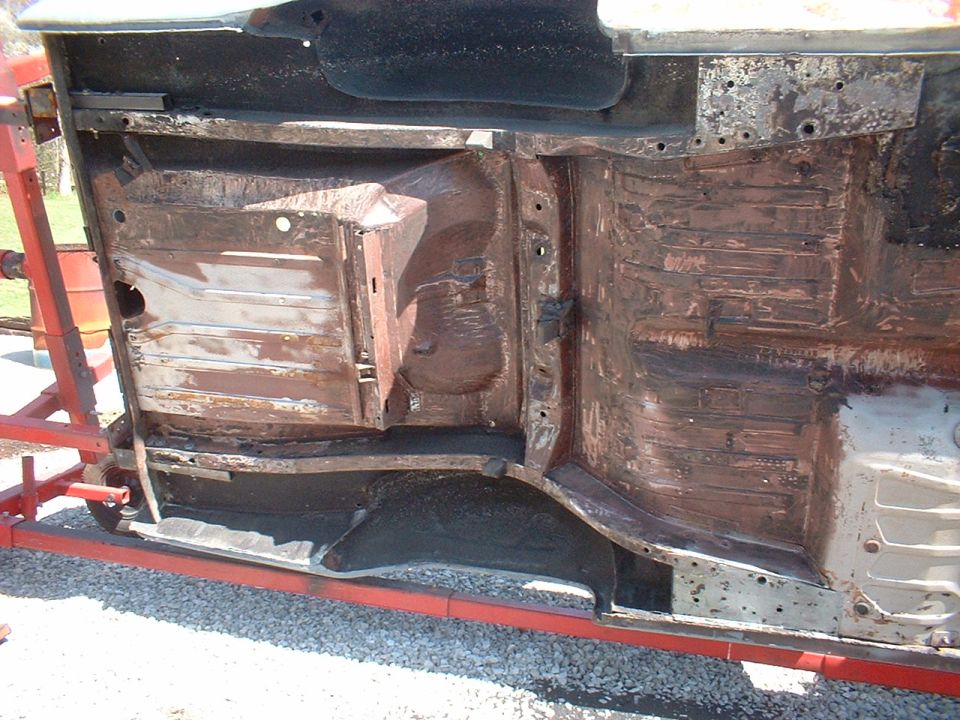 Car chassis on a red rotisserie lift, showing extensive rust and damage to the undercarriage