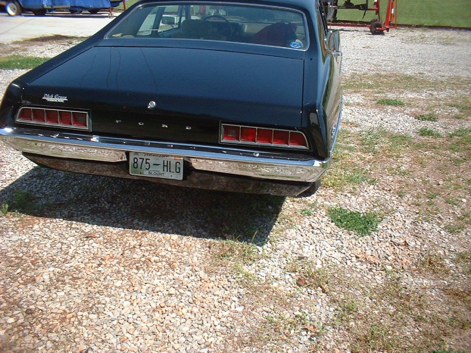 Rear of a dark classic Ford hardtop on gravel with chrome bumper and Tennessee plate 875-HLG