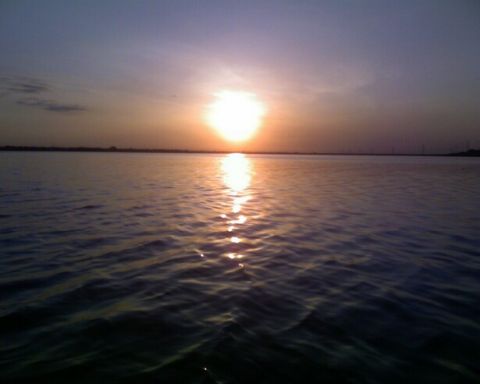 1953 Ford Mainline - The sun casts a bright reflection on the water during a peaceful sunset.