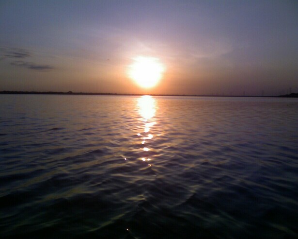 Sun setting over a calm body of water, reflecting light