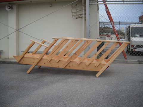 1986 Ford Bronco - Wooden stairs are positioned on an asphalt surface, with a white truck and an orange ladder visible in the background behind a chain-link f…