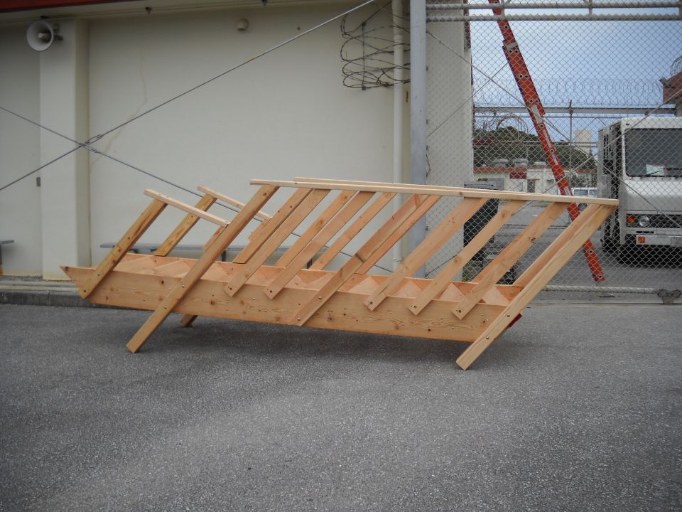 Wooden stairs on asphalt, with a white truck and a ladder visible behind a fence