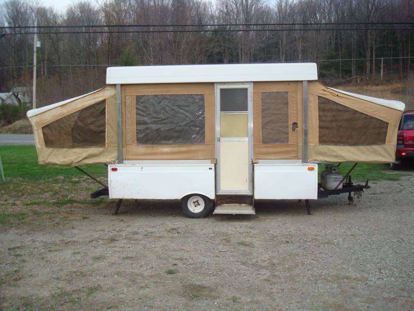 Pop-up camper with tan canvas sides and white body, parked on gravel