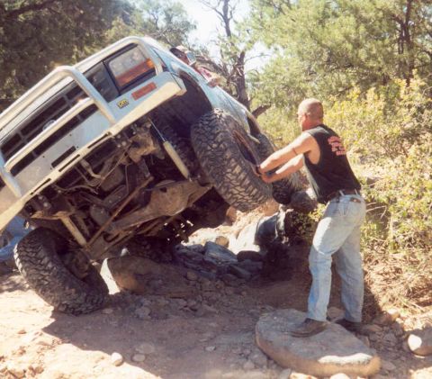 2002 Ford F-350 - A man helps maneuver a silver off-road truck over challenging terrain.