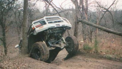 2002 Ford F-350 - An off-road vehicle is stuck between trees, its front end tilted upwards and engine compartment visible.