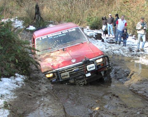 2002 Ford F-350 - A red off-road vehicle is stuck in a muddy trail with several people watching.