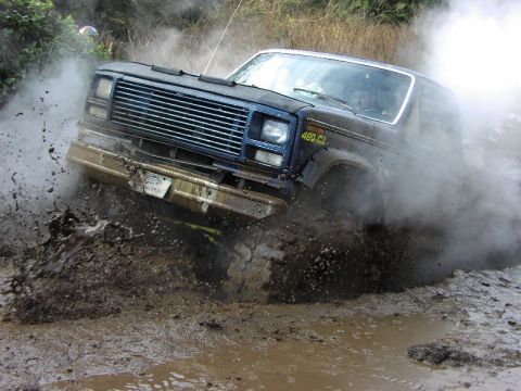2002 Ford F-350 - This blue off-road truck navigates a muddy terrain, kicking up a significant amount of spray and steam.