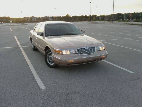 1996 Mercury Grand Marquis - A tan Mercury Grand Marquis is parked in a vacant lot during the day.