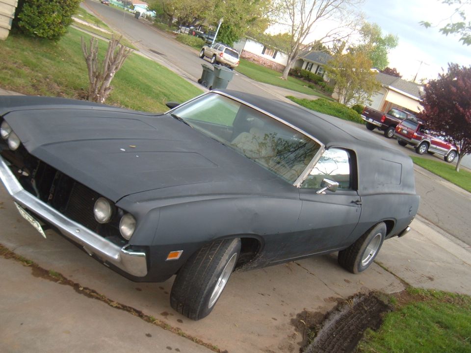 Matte-black two-door car, front 3/4 view, on suburban driveway