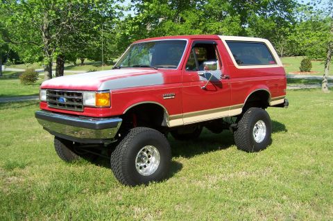 1990 Ford Bronco - This lifted 1990 Ford Bronco features a two-tone red and tan paint scheme with chrome wheels and large off-road tires.