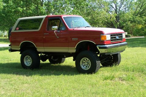 1990 Ford Bronco - Lifted 1990 Ford Bronco with aftermarket wheels and tires sits on a grassy lawn.