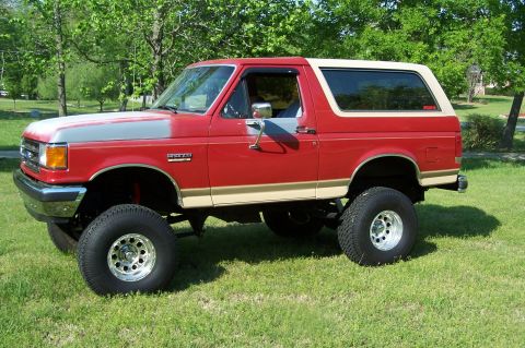 1990 Ford Bronco - This lifted Ford Bronco is parked on a grassy lawn with trees in the background.