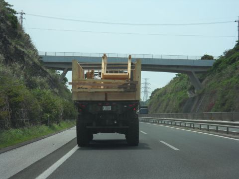 1986 Ford Bronco - A military truck transports a load of lumber on a highway under an overpass.