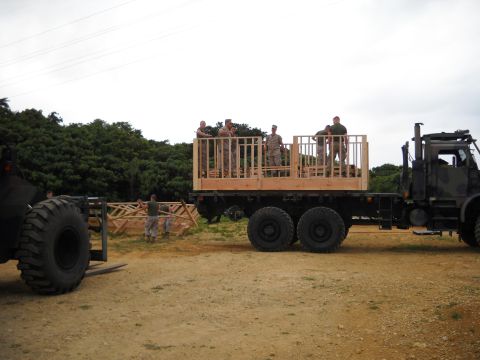 1986 Ford Bronco - Military personnel are working with a flatbed truck and a forklift to move a wooden structure.