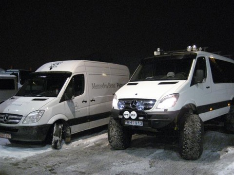 1990 Ford Bronco - Two white Mercedes-Benz Sprinter vans are parked in a snowy area at night, with one appearing to be an off-road modified version.