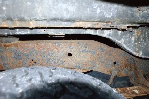 1979 Ford Bronco - The underside of a vehicle shows significant rust on the frame and chassis components, with a tire visible.