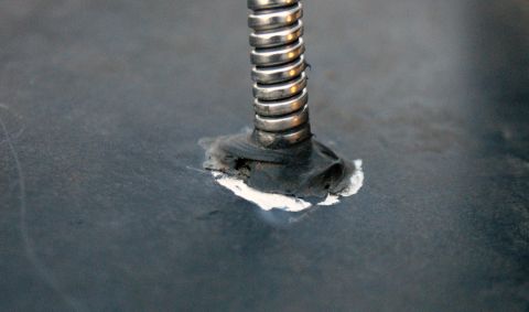1979 Ford Bronco - A close-up view of a metal spring and its mounting on a dark surface, with visible repair work.