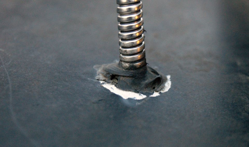 Metal spring with a rubber seal attached to a dark, textured surface, showing signs of repair