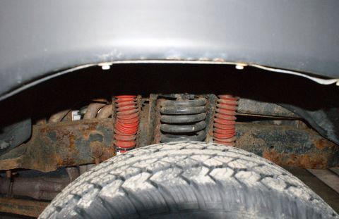1979 Ford Bronco - Front suspension and tire detail, showing red shock absorbers and rusty frame components.