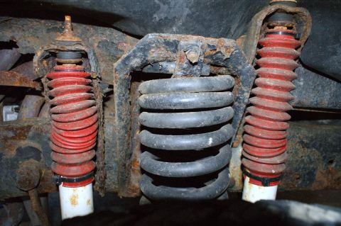 1979 Ford Bronco - The underside of a vehicle shows heavily rusted suspension components with red shock absorber boots.