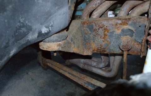 1979 Ford Bronco - Close-up view of heavily rusted vehicle undercarriage components, including the frame and exhaust manifold.