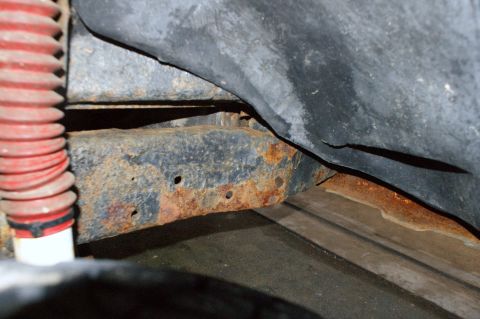 1979 Ford Bronco - Close-up view of a heavily rusted vehicle frame and a red suspension component, with 'SUPERMOTORS.NET' visible at the bottom.