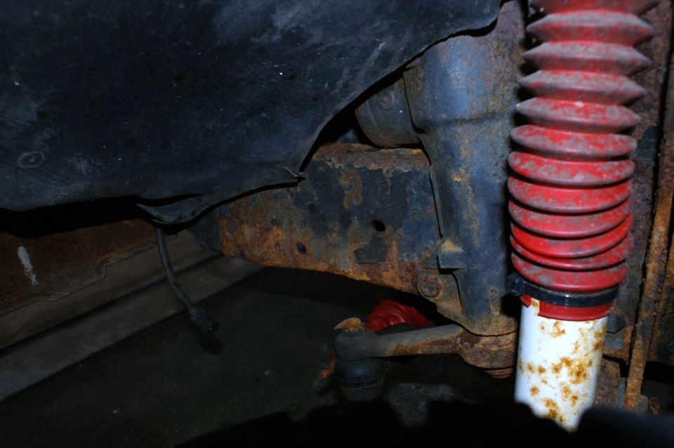 Rusted frame and red-booted shock absorber on a vehicle underside