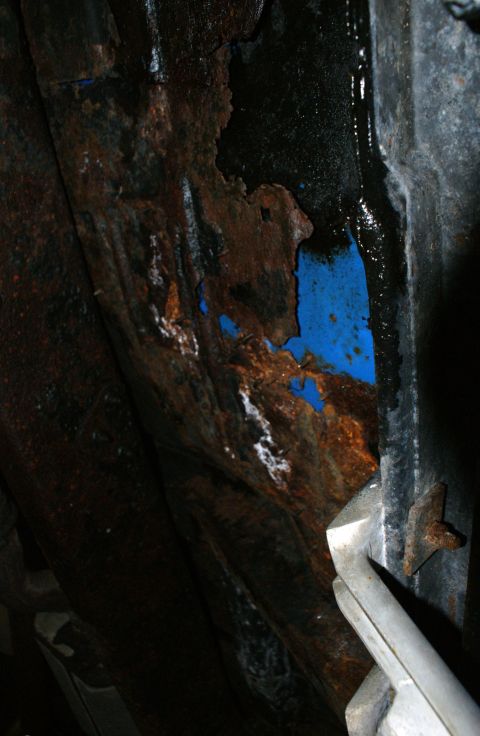 1979 Ford Bronco - Close-up of heavily rusted metal with patches of blue paint visible, likely from underneath a vehicle.