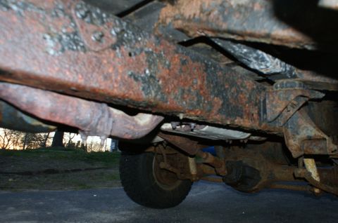1979 Ford Bronco - Underside view of a heavily rusted vehicle frame, showing exhaust pipes and suspension parts.