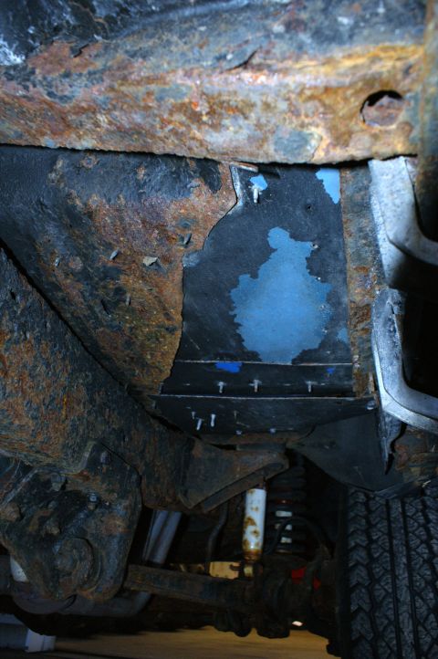 1979 Ford Bronco - The heavily rusted undercarriage of a vehicle shows signs of repair with blue paint and visible suspension parts.