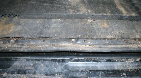 1979 Ford Bronco - The underside of a vehicle shows wear and tear with visible rust and dirt accumulation on its metal components.