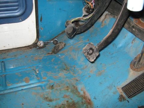 1972 Ford F-250 - The interior floor of a vehicle shows pedals, a window crank, and exposed wiring.