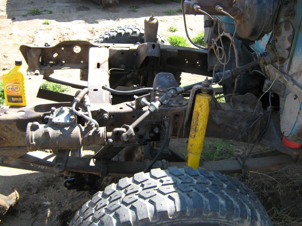 Truck frame and steering components mid-conversion with yellow shock and Pennzoil bottle