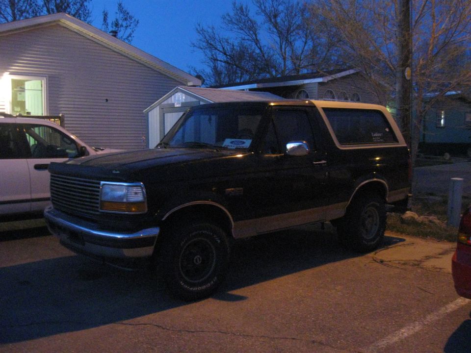 Black Ford Bronco with tan trim, parked in a driveway at dusk