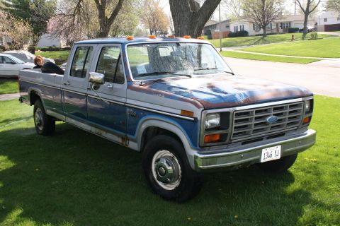 1985 Ford F-350 - This Ford F-350 pickup truck has a crew cab and dual rear wheels, with visible rust on the hood.