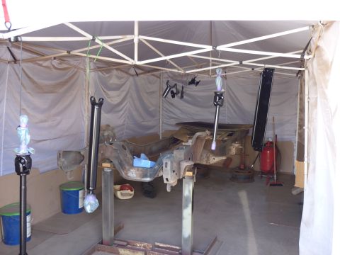 1984 Ford Bronco - The frame of a vehicle is suspended on stands within a temporary tent structure, likely for restoration or painting.