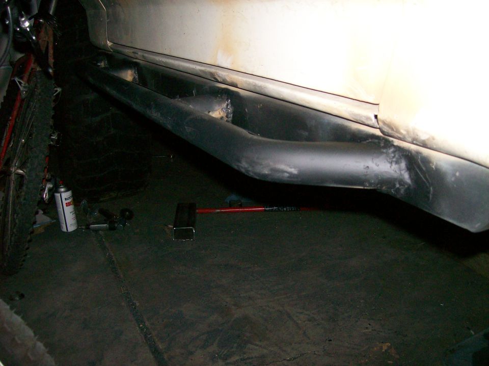 Side view of a vehicle's rocker panel with black tubular side steps and a tire visible on the left