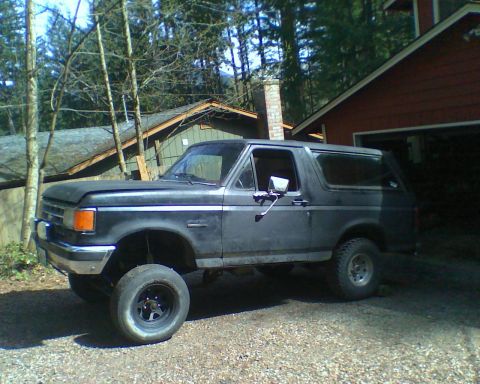 1987 Ford Bronco - This 1987 Ford Bronco is parked outside a garage with trees and a house in the background.