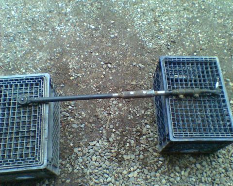 1987 Ford Bronco - A steering linkage part is shown resting on two blue crates on a gravel surface.