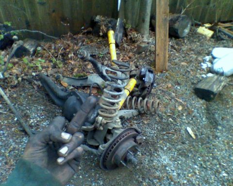 1987 Ford Bronco - Various vehicle suspension components, such as springs and brake assemblies, are piled on the ground amidst debris.