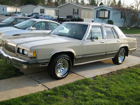 1988 Mercury Grand Marquis - A 1988 Mercury Grand Marquis is seen from the front-three-quarter angle, parked in front of mobile homes.