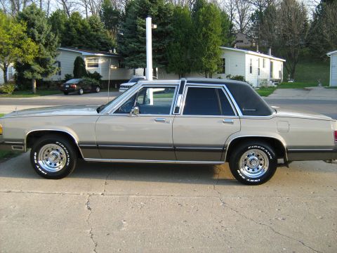 1988 Mercury Grand Marquis - A tan 1988 Mercury Grand Marquis is parked on a concrete driveway in front of a residential area.