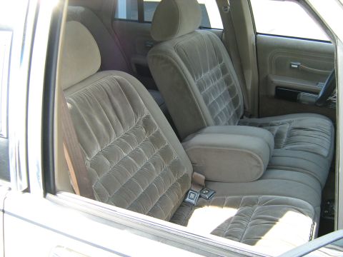 1988 Mercury Grand Marquis - The plush velour interior of a car features front bucket seats with a center armrest and console.