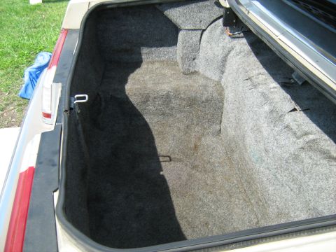 1988 Mercury Grand Marquis - The interior of a car trunk is shown with gray carpeting and a beige exterior.
