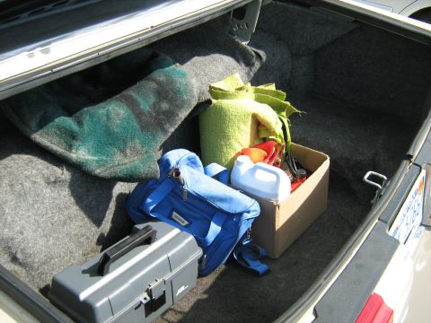 1988 Mercury Grand Marquis - The trunk of a car is filled with blankets, a toolbox, a blue bag, and a cardboard box containing various items.