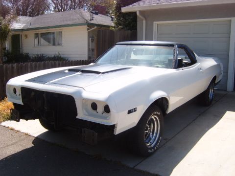 1973 Ford Ranchero - This white coupe utility is parked in a driveway in front of a garage and house.
