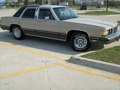 1988 Mercury Grand Marquis - A 1988 Mercury Grand Marquis sedan is viewed from the front three-quarter angle, showing its two-tone paint and chrome accents.