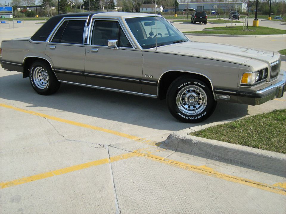 Tan and dark brown 1988 Mercury Grand Marquis sedan parked on concrete with yellow lines, chrome wheels, and a black vinyl roof