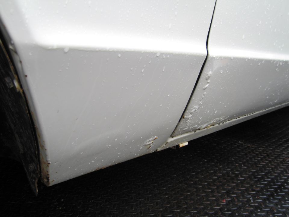 White car door bottom with rust and water droplets. Diamond plate surface below