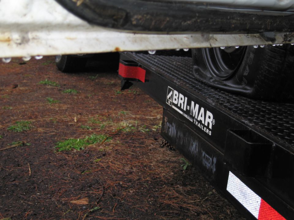 Close-up of a Bri-Mar trailer deck with a tire visible, showing water droplets on a white surface above